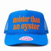 A bright blue trucker hat with orange embroidered text reading 'moister than an oyster' on the front panel, plus a pink-and-white lip-shaped sticker on the brim, shown on a white background.