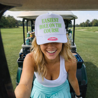 Woman wearing a cap with 'Easiest Hole on the Course' text in a golf setting