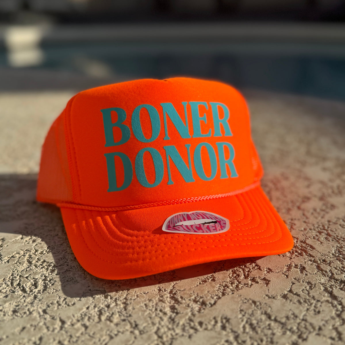 Orange cap with 'BONER DONOR' text on a textured surface