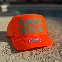 Orange cap with 'BONER DONOR' text on a textured surface