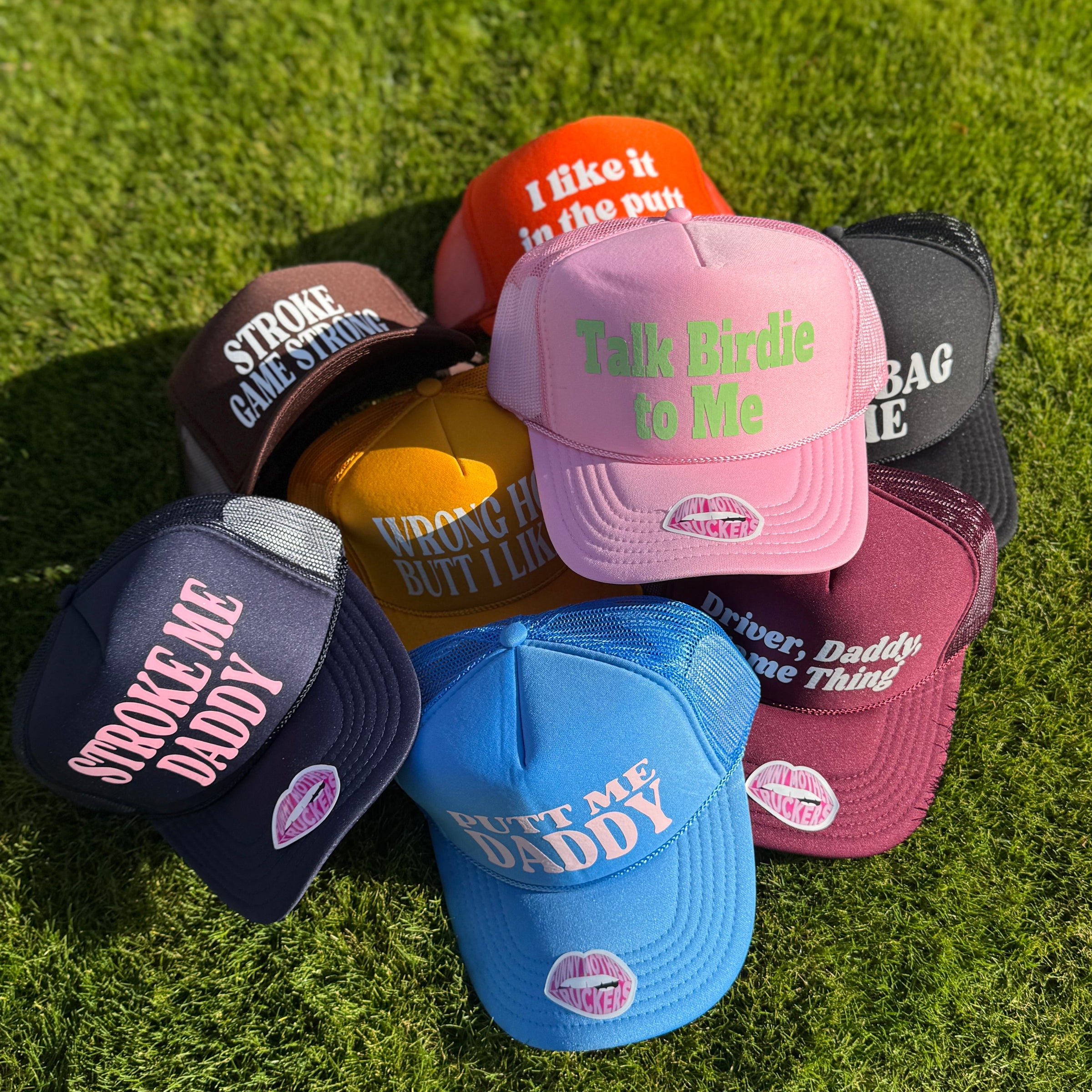 Collection of colorful caps with various text designs on a grassy background with golf sayings