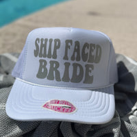 Gray cap with 'SHIP FACED BRIDE' text on a towel by a pool