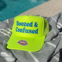 Yellow cap with 'Boozed & Confused' text on a towel by a pool