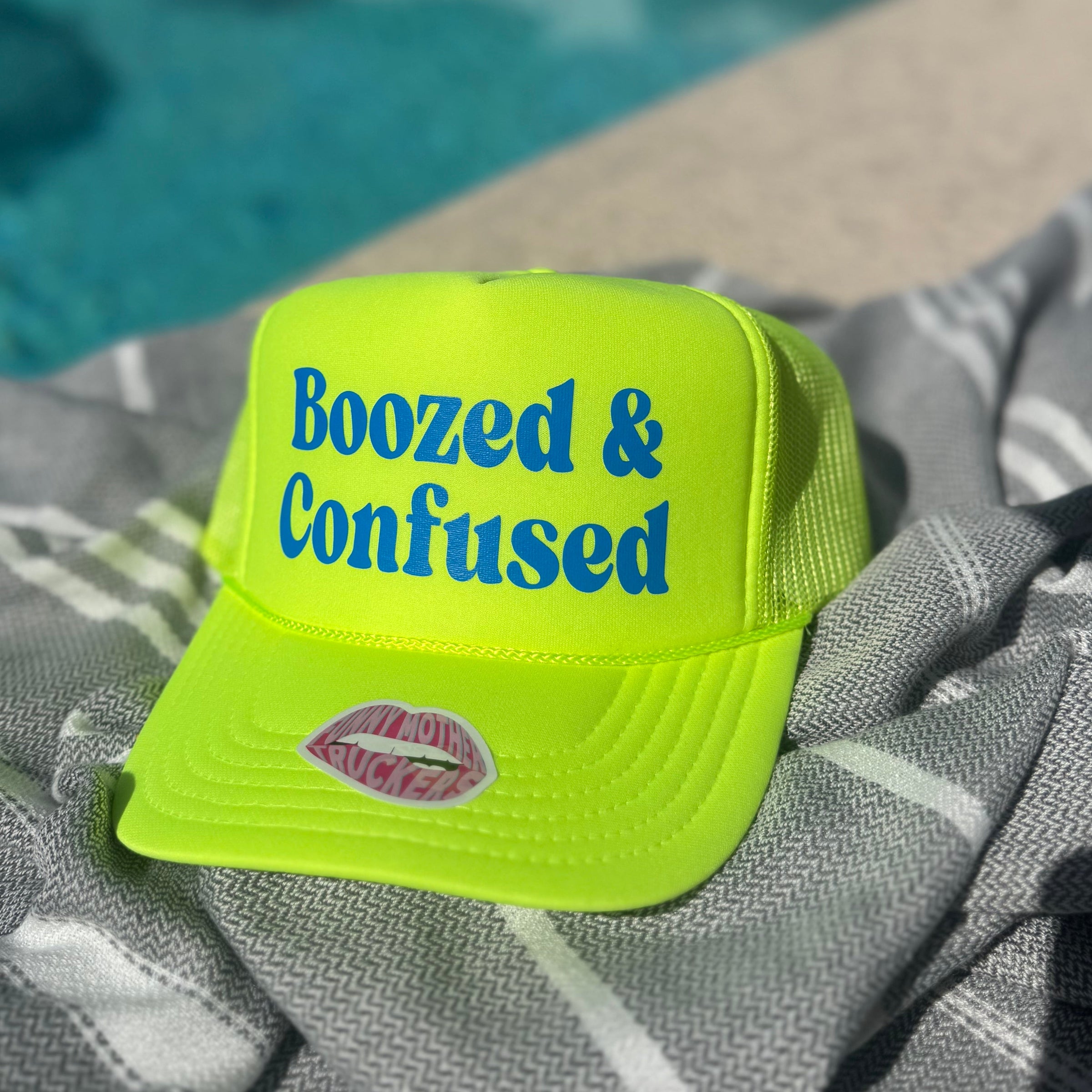 Yellow cap with 'Boozed & Confused' text on a towel by a pool