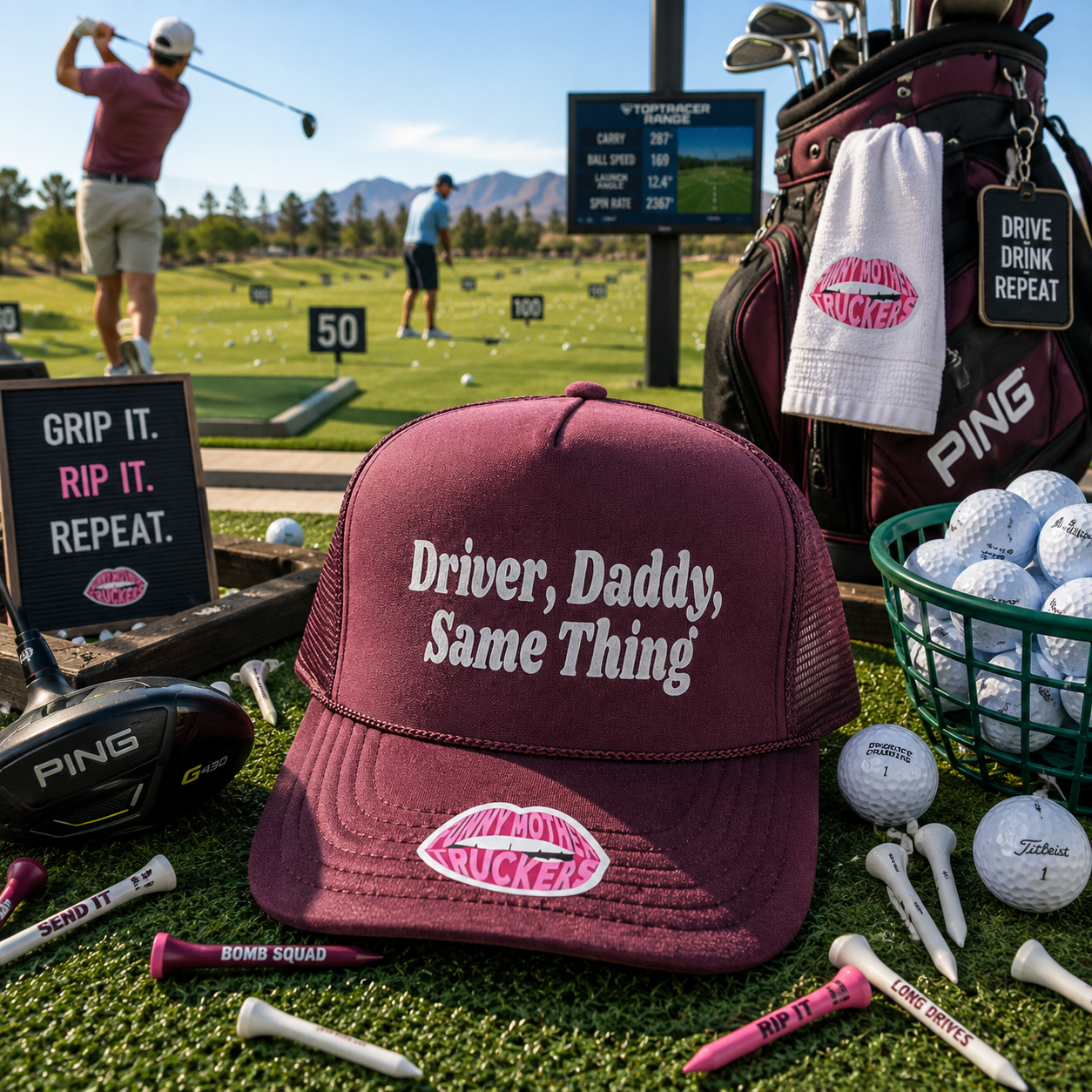 A maroon trucker hat with white embroidered text reading 'Driver, Daddy, Same Thing' and a pink lips logo patch, displayed on a golf course driving range with golf bags, balls, tees, and other golf props around it.