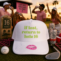 A white trucker hat with green text reading 'if lost, return to hole 16' and a pink lip graphic on the brim, styled on a golf course at sunset with people, beer cans, a golf ball, and a golf club in the background.